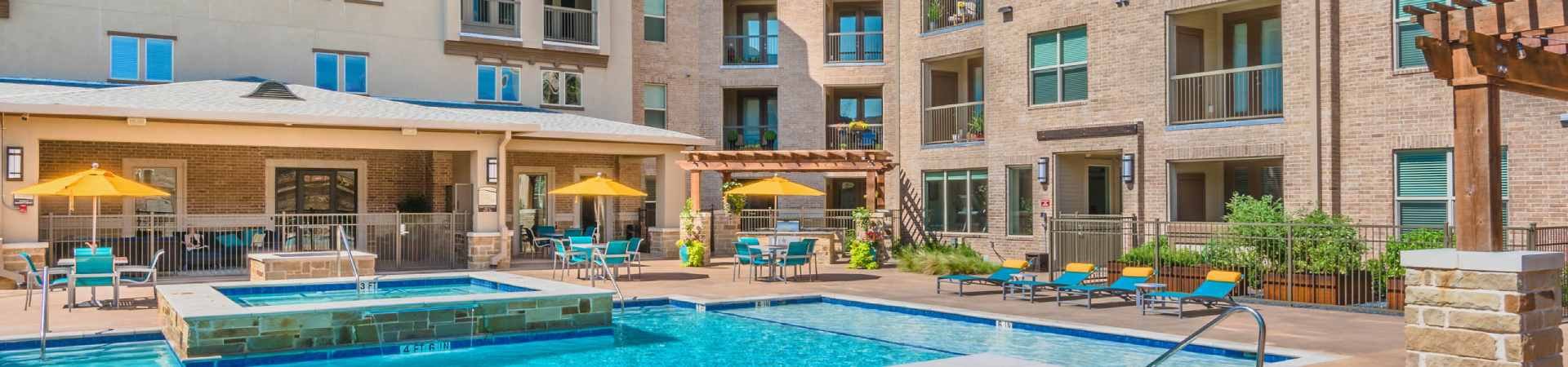 A large swimming pool surrounded by a patio with chairs and umbrellas. at Atlas Point at Prestonwood Apartments , Carrollton, 75010